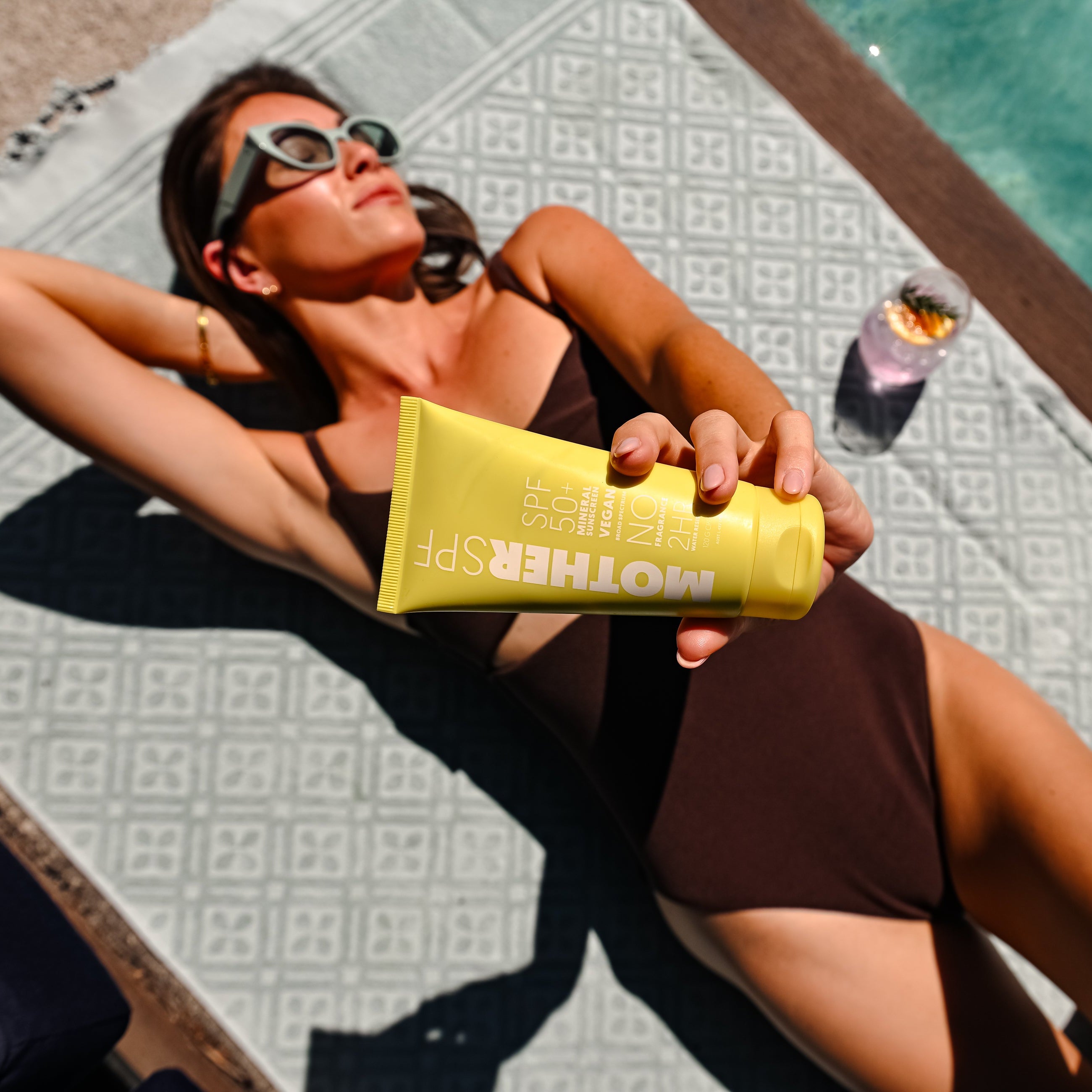 Woman lying by a pool holding a yellow container labeled 'Mother Spf'.